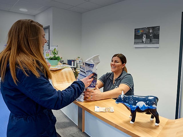 Eine Kundin steht an der Rezeption und bekommt von einer Tierpflegerin eine Packung Futter ausgehändigt.