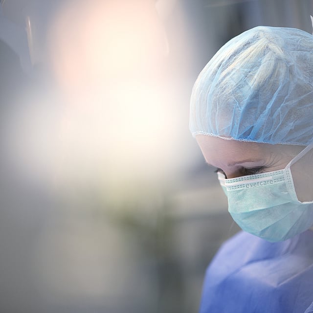 Eine Person, die eine OP-Kappe und eine Maske trägt.