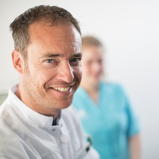 Eine lächelnde Person mit einer Krankenschwester hinter sich.