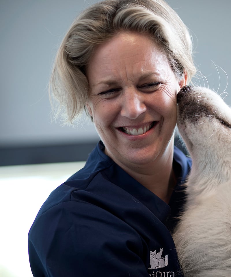 Eine Tierärztin hält neben sich einen weißen Hund im Arm. Sie lacht in die Kamera, während er an ihrem Gesicht riecht.