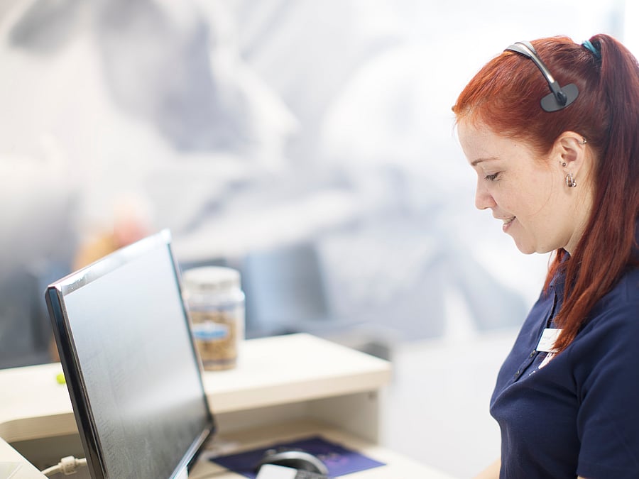 Eine Fachangestellte sitzt vor dem Computer und hat ein Headset auf.