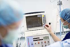 Ein Monitor zeigt den Herzrhythmus während einer OP an. Eine Tierärztin dreht an einem Knopf.