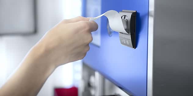 Eine Hand zieht einen Zettel aus einem Automaten.