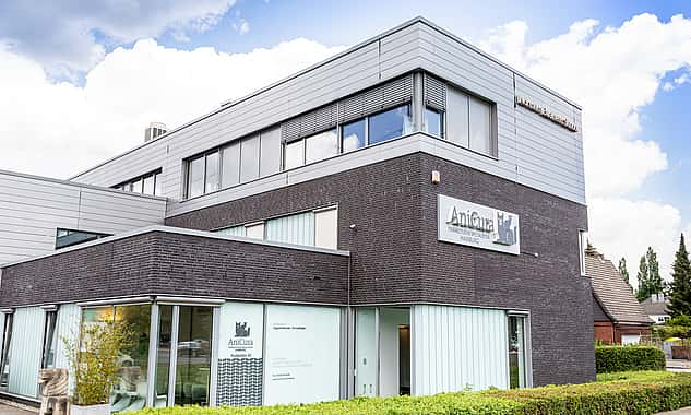 Das Haus, in dem sich die Praxis befindet, ist modern und hat große Fenster. Drum herum ist eine grüne Hecke.