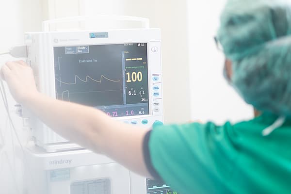 Eine Person in Kitteln und OP-Haube, die an einem medizinischen Monitor arbeitet.
