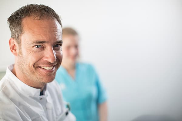 Eine lächelnde Person mit einer Krankenschwester hinter sich.