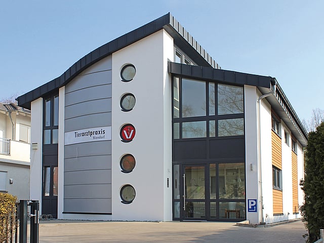 Das Haus, in dem sich die Praxis befindet, ist groß und modern. Der Eingang ist mit einer ganzen Glaswand ausgestattet.