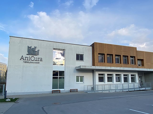 Die Praxis ist in einem sehr großen und modernen Gebäude aus Beton mit Holzelementen. An der Wand ist ein großes Anicura-Logo abgebildet.
