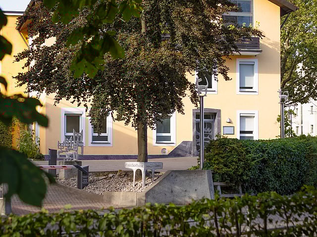 Eine Tierärztin kniet auf dem Boden. Links von ihr sitzt ein schwarzer Hund, den sie anschaut und rechts sitzt eine Katze, die sich an sie anschmiegt.