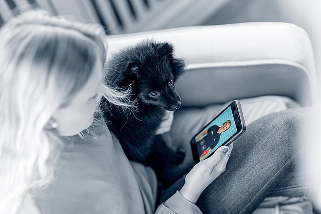 Eine Person, die mit einem Hund und einem Tablet auf einer Couch sitzt.